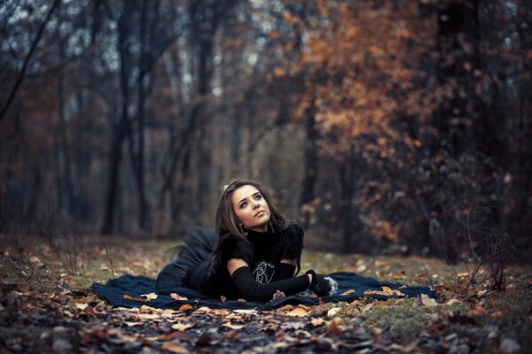 The girl lies on the leaves in the autumn forest