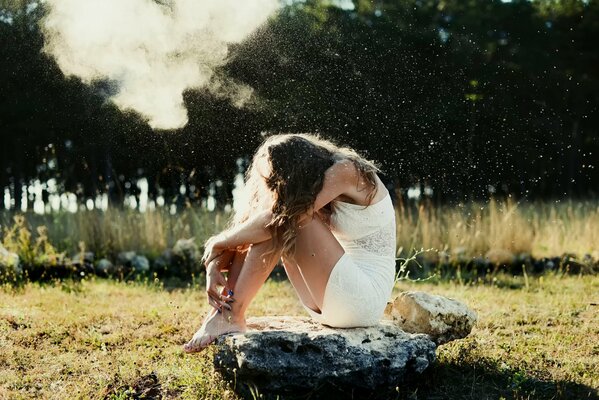 Chica de blanco se sienta en una piedra