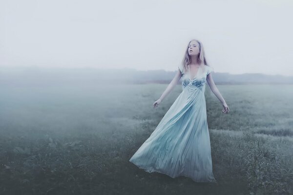 Ein Mädchen in einem langen Kleid steht im Nebel auf einem Feld