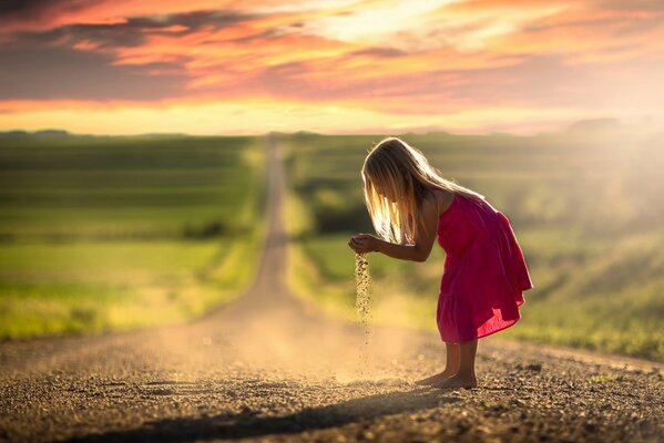 Little girl playing with sand on the road