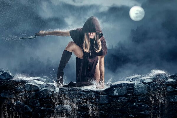 La jeune fille dans un manteau de danse avec un couteau sous la lune