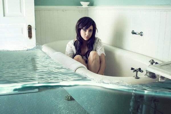 The girl is sitting in the tub and there is a lot of water