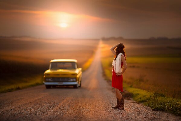 La jeune fille au coucher du soleil sur la route. La machine