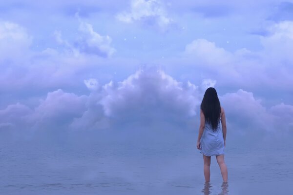 The girl is standing in the water under the clouds