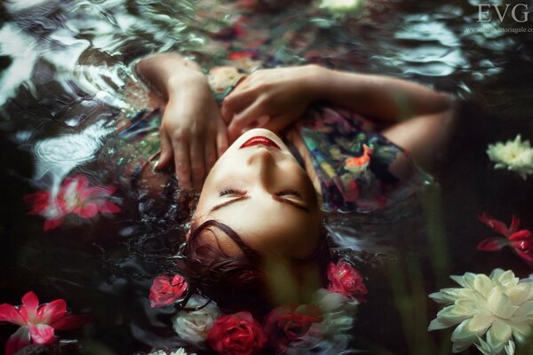 La chica que se acuesta en el agua con flores