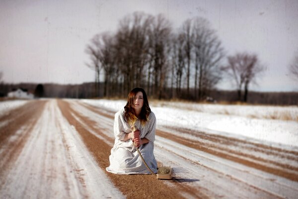 La jeune fille avec un téléphone filaire sur une route enneigée