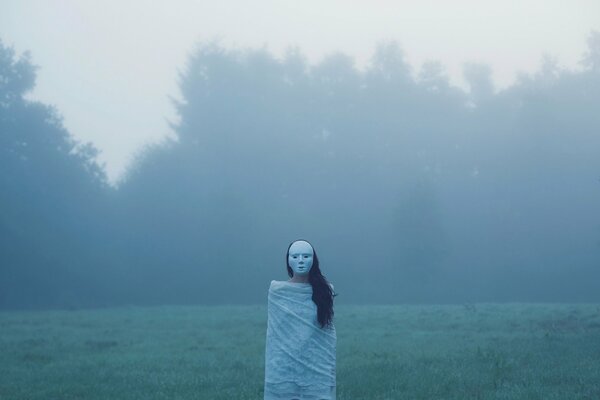 A girl in a field, in a mask and a sheet