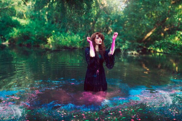 Sesión de fotos de una chica en un vestido oscuro y con pintura en las manos en el agua