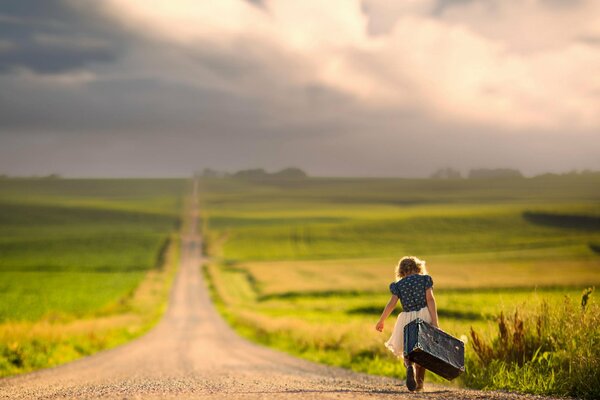 Una ragazza con una valigia cammina lungo la strada