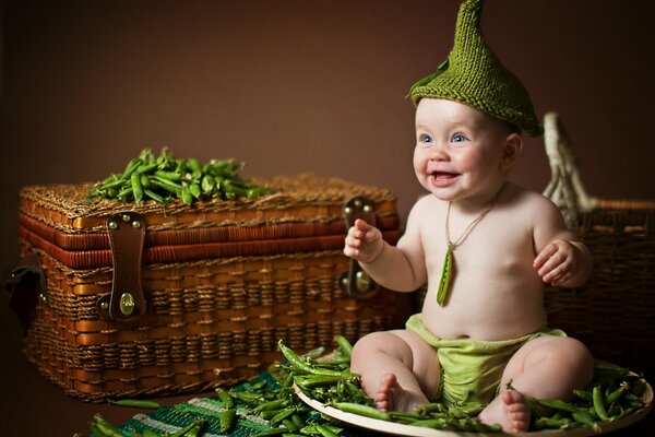 A cheerful kid is sitting on a plate with peas