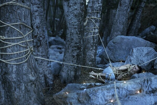 Mann liegt an Bäumen auf Steinen im Wald gebunden