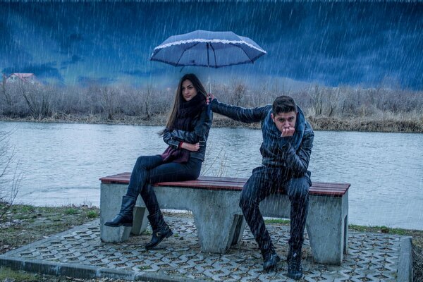 A guy holds an umbrella for a girl while he is in the rain