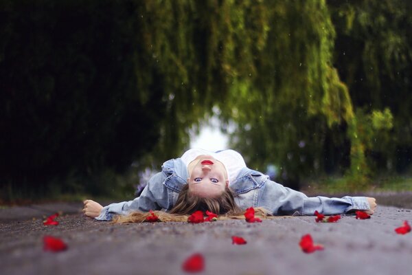 Una niña yace en el camino en pétalos de flores