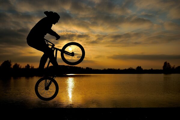 A man on a bike at sunset jumping by the lake