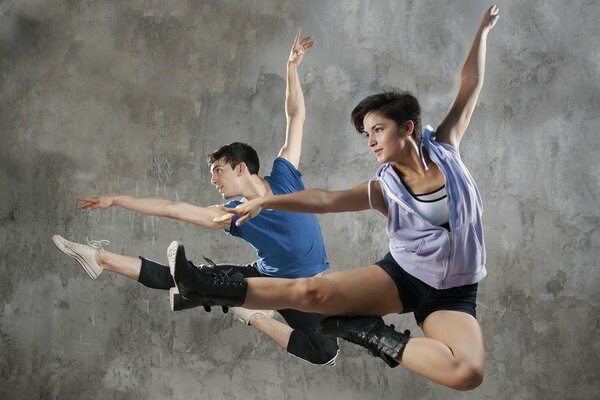 Two dancers jump on a gray background