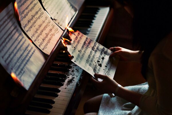 Una chica se sienta detrás de un piano y quema una hoja con notas