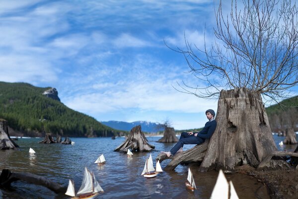 Der Kerl sitzt lehnend auf einem Baum und schaut auf die Boote