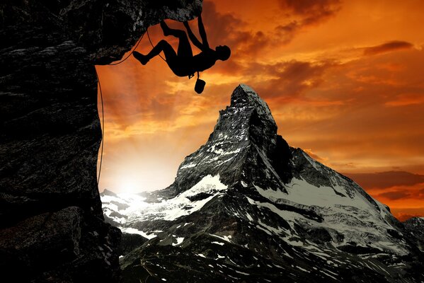 A climber climbs a steep snow-covered cliff against the background of an orange sunset