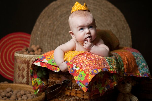 The baby on the blanket was thinking with a finger in his mouth