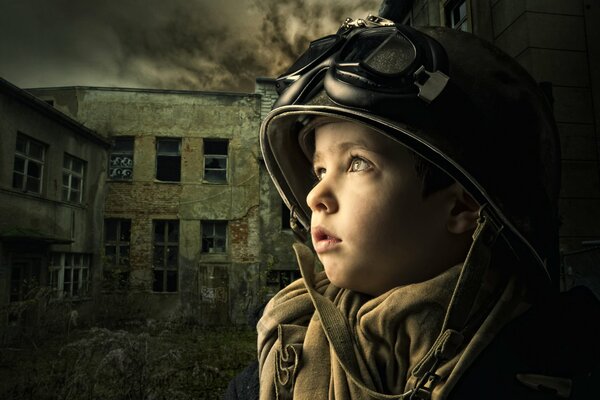 Un niño pequeño con un casco y un abrigo se encuentra entre una casa destruida en el fondo de nubes oscuras