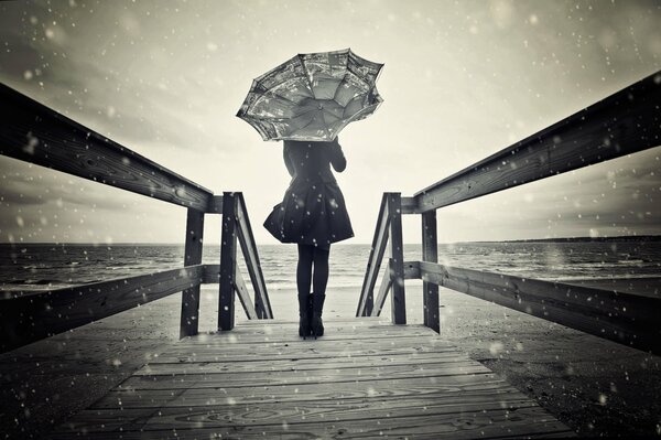 Mädchen steht auf einer Brücke unter dem Schnee mit einem Regenschirm in den Händen