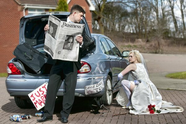 The girl is fixing the car and the guy is reading the newspaper