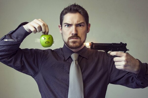 Un hombre con una pistola y una manzana. Foto puesta en escena