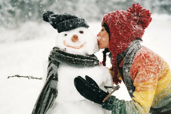 La ragazza bacia il pupazzo di neve che ha modellato dalla neve in inverno