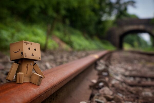 Danbo is a cardboard man sitting on the rails of a railway going into the distance