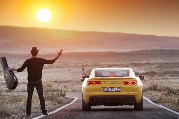 Un chico con una guitarra en la carretera cerca de un auto que se fue