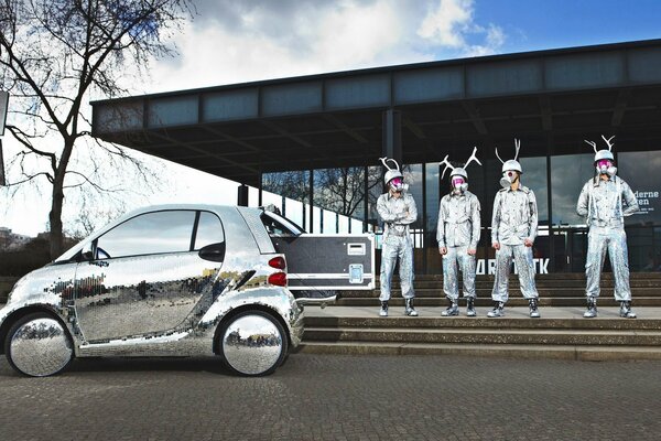 Menschen in glänzenden Overalls in der Nähe eines silbernen Autos