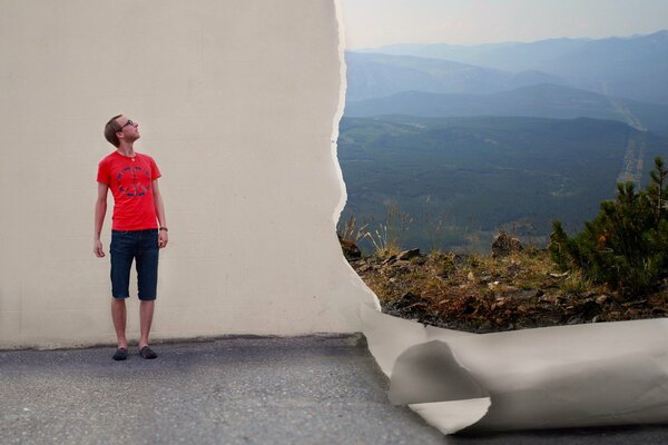 A guy in a red T-shirt looks at the sky near a white wall