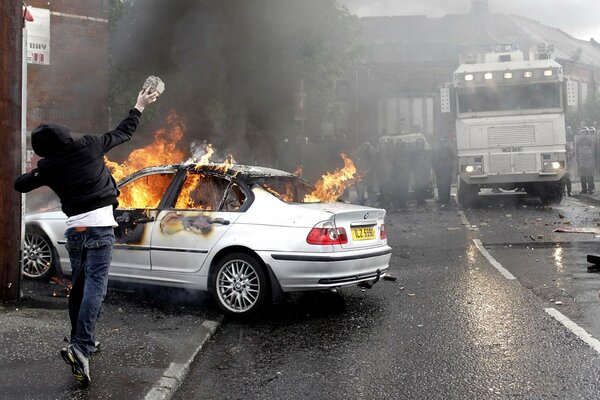 A bully throws a stone at a burning car