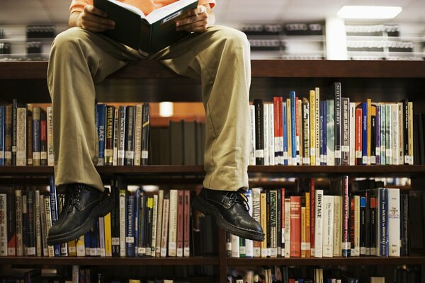 A man sits on a shelf in the library and reads