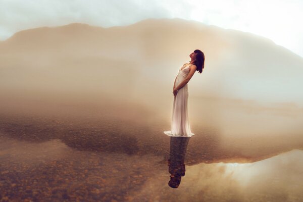 A girl in a dress stands in the middle of a lake