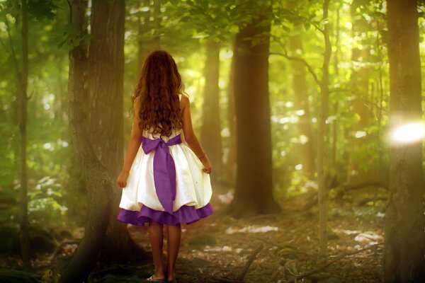 A girl in a beautiful dress is standing with her back in the forest