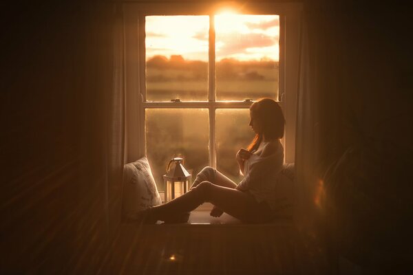 Fille sur le rebord de la fenêtre sur fond de coucher de soleil