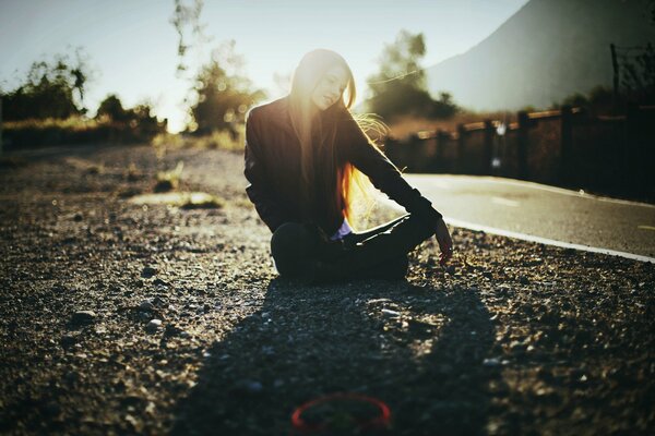 Chica se sienta en la carretera y el sol juega en su pelo