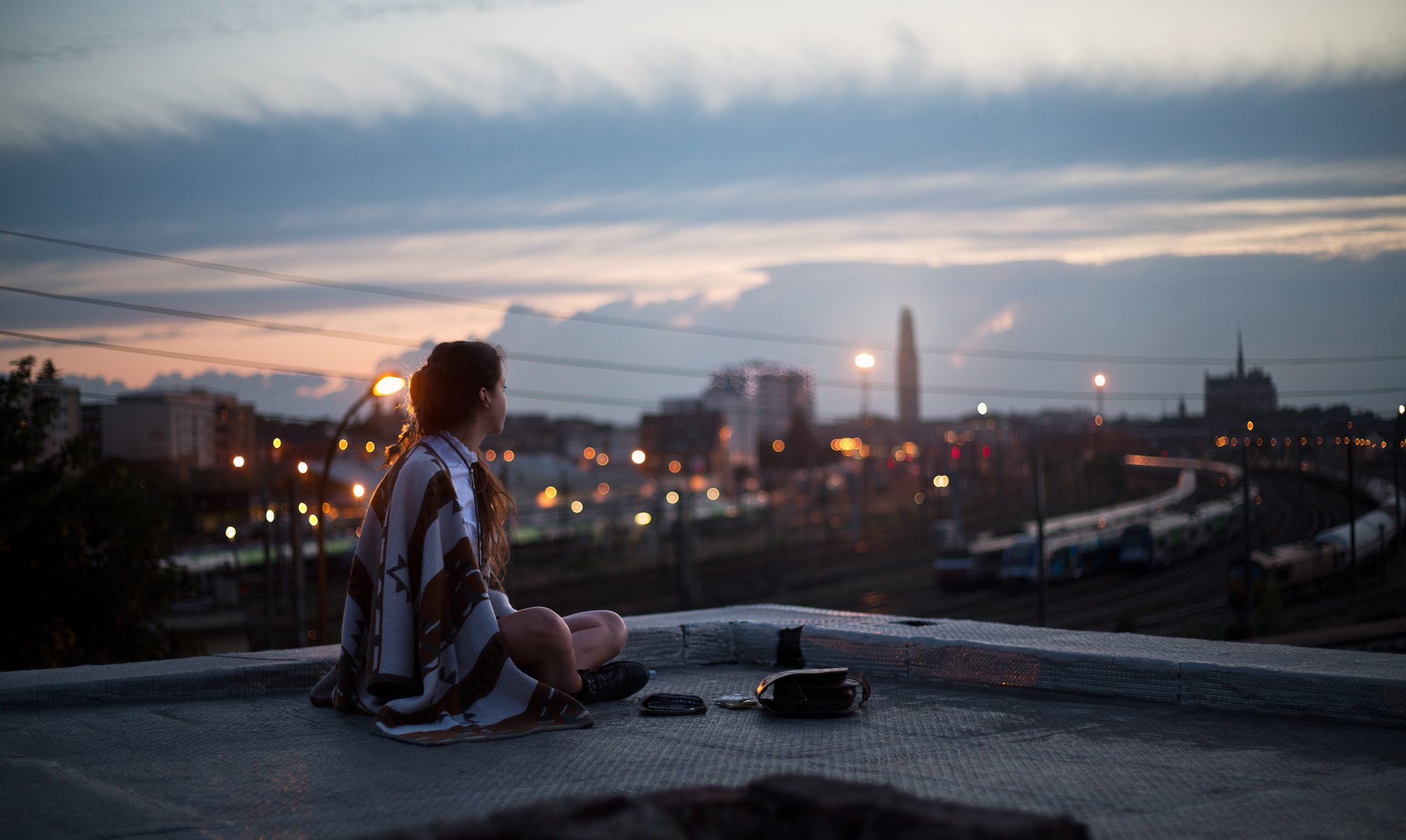 girl night roof sitting plaid blanket watches town street lights lamp