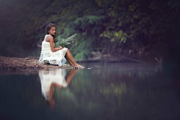Fille triste assis sur le rivage avec un bouquet de fougères