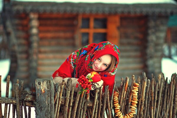 Mädchen in einem russischen Kopftuch mit Lamm auf dem Hintergrund einer Hütte