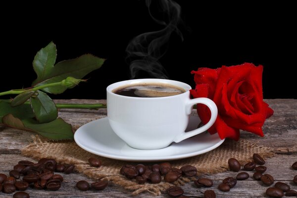 A cup of fragrant coffee on the table with a red rose