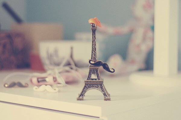 A small Eiffel Tower on a table with a hat and mustache