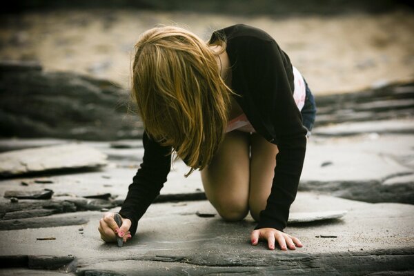 A girl writes with chalk on a stone