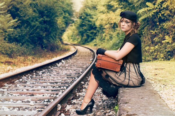 Jeune fille dans un chapeau et une valise dans les mains est assis près du chemin de fer