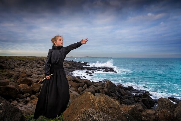 A girl in a dark dress on a rocky seashore