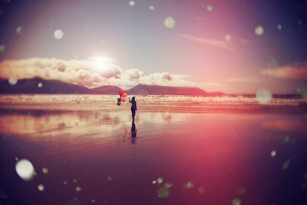 A girl with balloons walks along the seashore