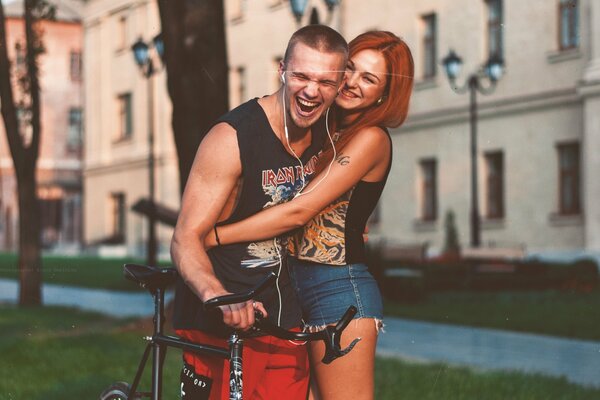 Chica pelirroja en pantalones cortos abraza a un chico con una bicicleta en auriculares