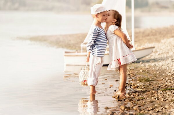 A girl kisses a boy in a sailor suit on the beach