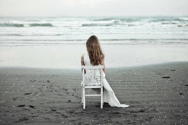 A girl in white is sitting on a chair in front of the ocean